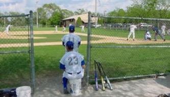 People in blue and white uniforms play baseball on a grassy field.